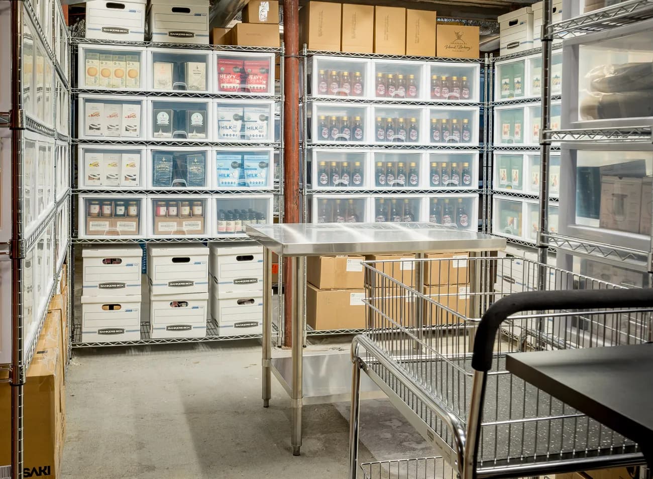 Shelves of labelled bins and cartons in Mellifera's stock room, with a steel packing table at the centre